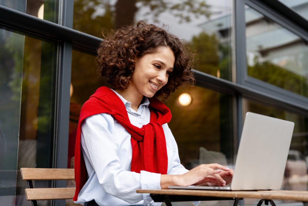Quel expert-comptable en ligne choisir ? smiling woman working on laptop at outdoor cafe wearing casual red sweater